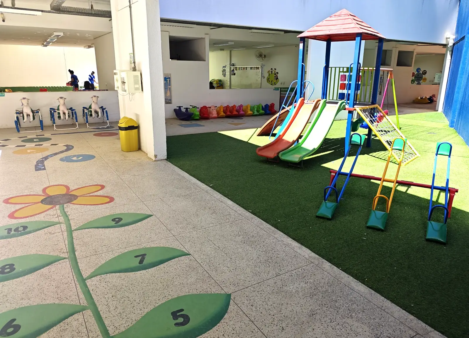 Escorregadores coloridos sobre grama sintética, ao lado das salas da Educação Infantil