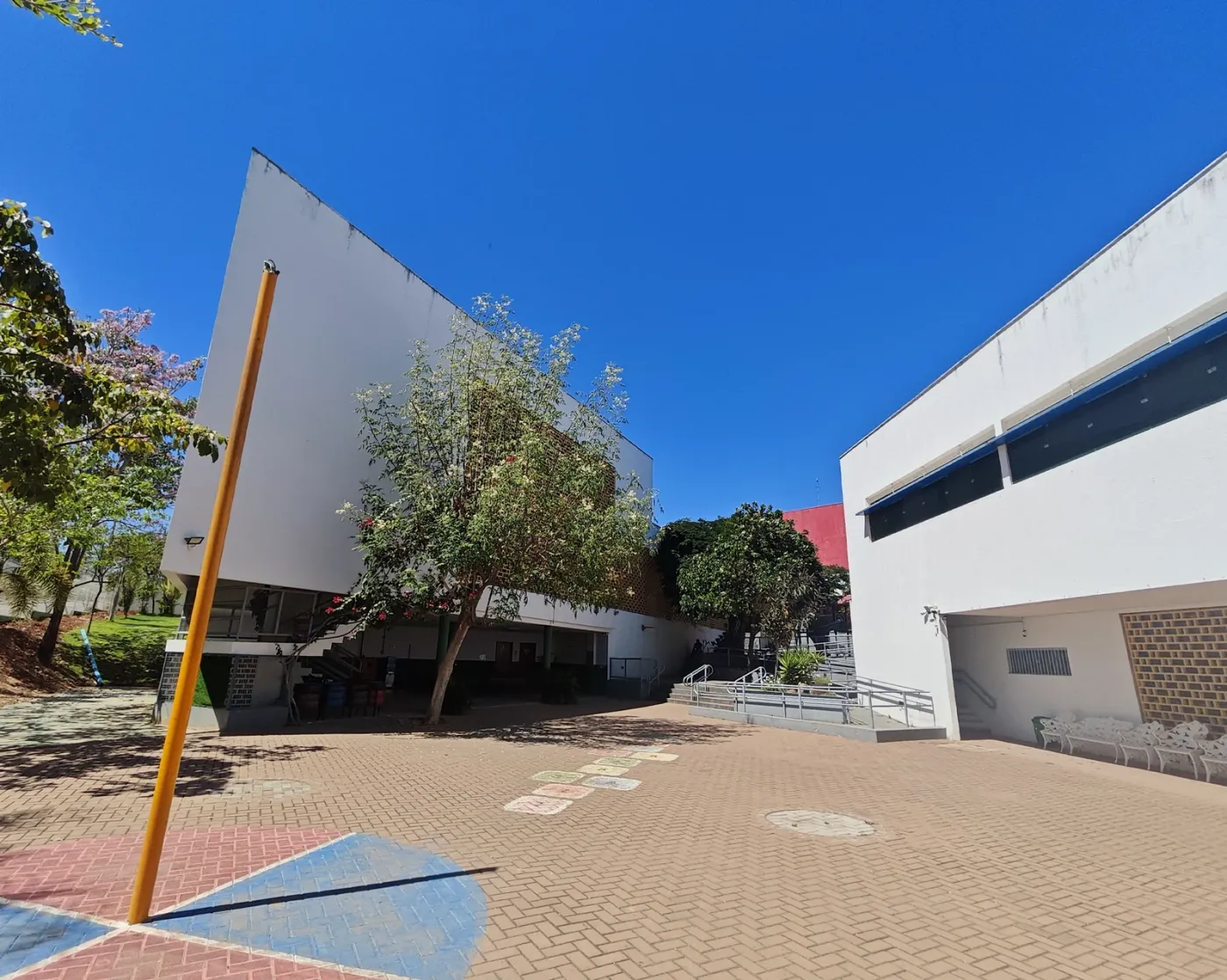Pátio do Colégio Domum com árvores, piso de tijolinhos e os prédios da escola