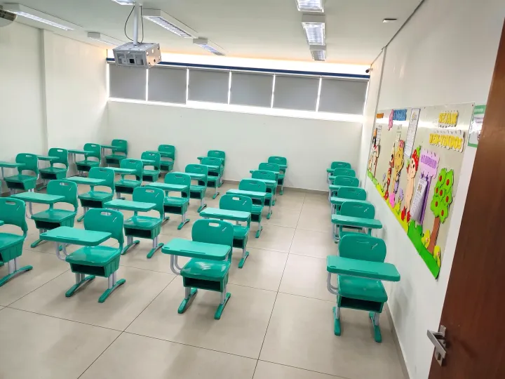 Sala de aula com carteiras verdes, janelas e projetor