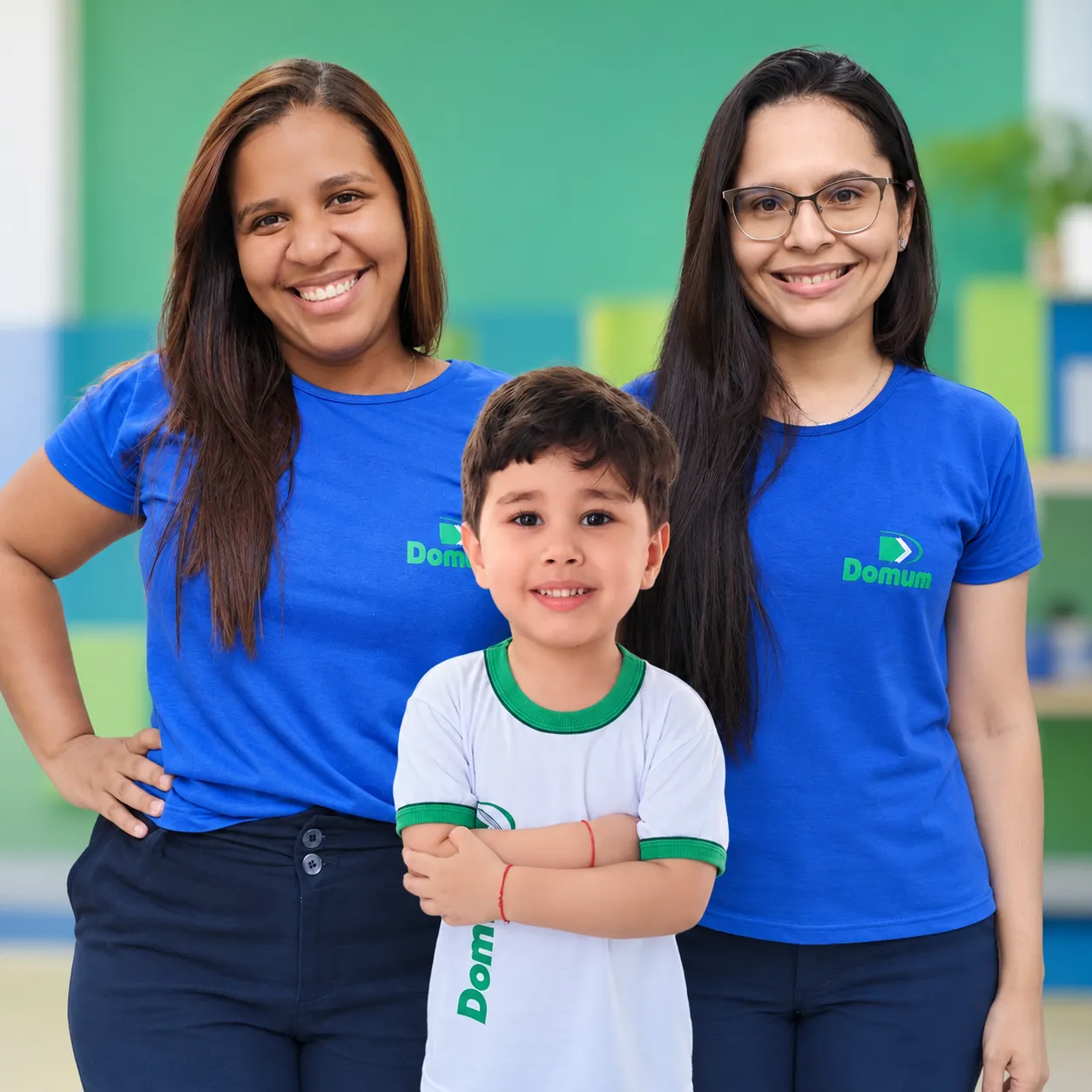 Duas professoras do Colégio Domum, de camiseta azul, com um aluno da Educação Infantil entre elas